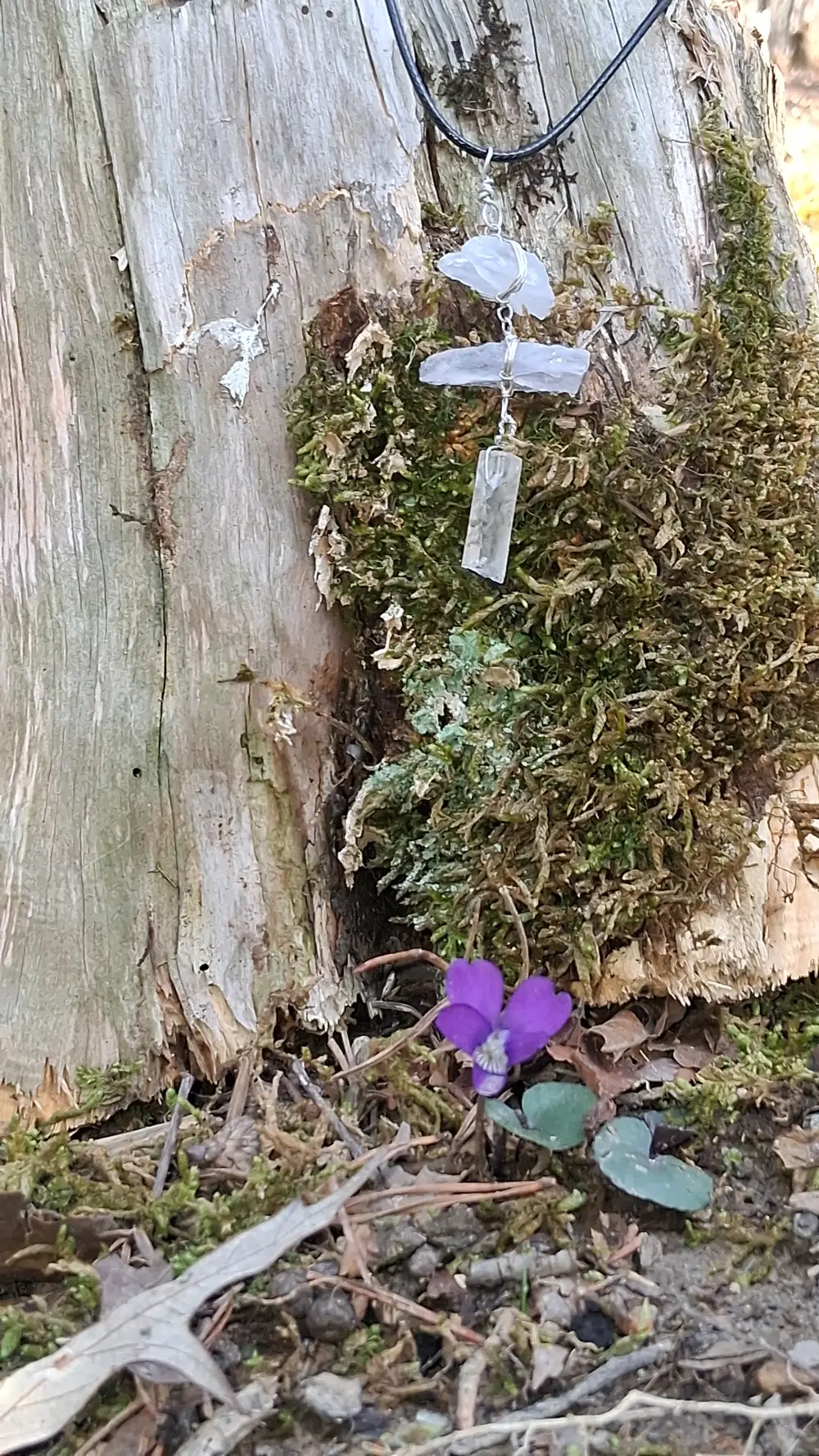 A handmade pendant rests on weathered wood from a recent woodland walk